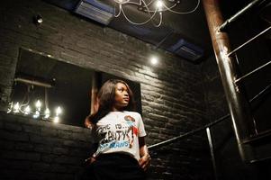 stijlvolle Afro-Amerikaanse vrouw in bedrukt t-shirt poseerde binnen stalen trappen. foto