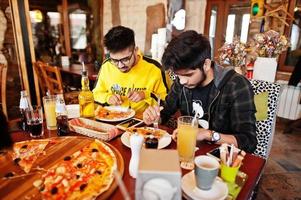 Aziatische vrienden jongens die pizza eten tijdens het feest bij pizzeria. gelukkige indiase mensen die samen plezier hebben, Italiaans eten en op de bank zitten. foto