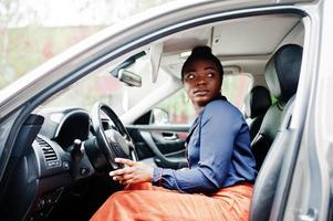 rijke zakelijke afrikaanse vrouw zit op de bestuurdersstoel bij zilveren suv-auto met geopende deur. foto