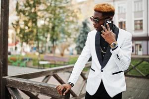 chique knappe Afro-Amerikaanse man in wit pak met mobiele telefoon bij de hand. foto