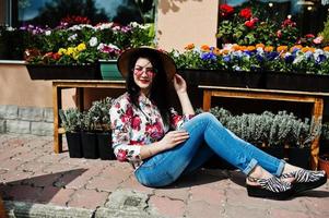 zomer portret van brunette meisje in roze bril en hoed tegen bloemenwinkel. foto