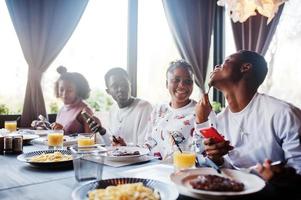 gelukkige afrikaanse vrienden zitten, kletsen in café en eten eten. groep zwarte mensen die in restaurant samenkomen en dineren. foto