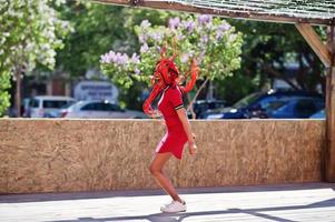 schattig en slank Afrikaans Amerikaans meisje in rode jurk met dreadlocks in beweging met plezier op straat. stijlvol zwart model. foto