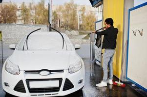 Zuid-Aziatische man of Indiase man die zijn witte transport op autowasserette wast. foto