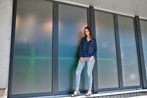 portret van jonge brunette meisje in blauw geruit overhemd tegen grote ramen. foto