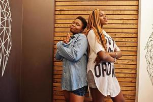 twee Afrikaanse dames in stijlvolle casual kleding poseren tegen houten muur. foto