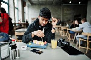 casual en stijlvolle jonge aziatische man met koptelefoon in café sushi eten. foto