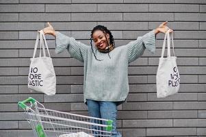 geen kunststof meer. Afrikaanse vrouw met winkelwagentje en eco-tassen poseerde buitenmarkt. foto