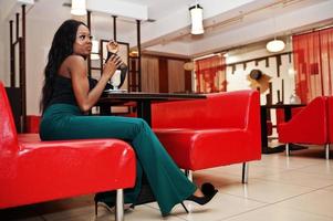 schoonheid slank afro-amerikaans model draagt een zwarte blouse en een groene broek met lange benen die latte drinkt in het chinees café. foto
