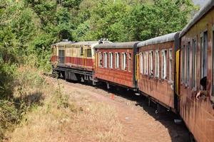 speelgoedtrein die zich op berghellingen beweegt, prachtig uitzicht, een zijberg, een zijvallei die zich op een spoorlijn naar de heuvel beweegt, tussen groen natuurlijk bos. speelgoedtrein van kalka naar shimla in india, indiase trein foto