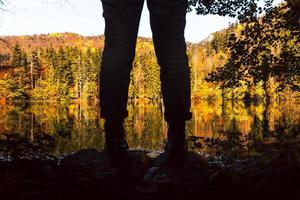 close-up lage hoek weergave silhouet van vrouwelijke benen en laarzen door schilderachtige meer met buiten in de herfst natuur. kleding in de natuur en herfstmodeconcept foto