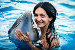 portret van een jonge blanke vrouw glimlach met dolfijn kijken naar de camera in het zwembadwater van batumi delphinarium. zwem met dolfijnervaringsconcept foto