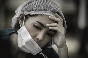 vermoeide depressieve vrouwelijke Aziatische scrubverpleegster draagt gezichtsmasker blauw uniform zit op de ziekenhuisvloer, jonge vrouwelijke arts gestrest van hard werken foto