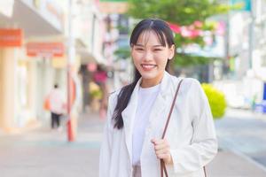 zelfverzekerde jonge zakelijke aziatische werkende vrouw die een wit overhemd en een schoudertas draagt, glimlacht gelukkig terwijl ze naar haar werk loopt op kantoor in de stad. foto