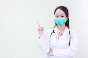 Aziatische vrouwelijke arts toont handpunt op witte achtergrond en draagt medisch gezichtsmasker en gezichtsschild in gezondheidszorgconcept foto