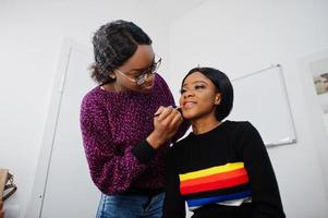 Afro-Amerikaanse vrouw die make-up toepast door visagist bij beauty salon. foto