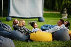 jonge multi-etnische groep mensen kijken naar film op poef in openluchtbioscoop. foto