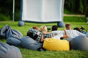 jonge multi-etnische groep mensen kijken naar film op poef in openluchtbioscoop. foto