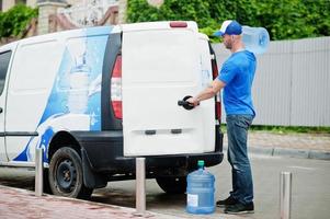 bezorger vooraan bestelwagen die flessen water levert. foto