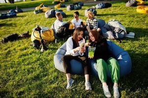 jonge multi-etnische groep mensen kijken naar film op poef in openluchtbioscoop. twee meisjes met mojitococktails. foto