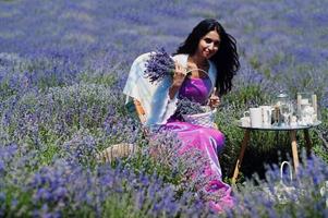 mooi indiaans meisje draagt saree india traditionele kleding zittend in paars lavendelveld met decor. foto