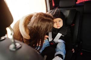 jonge moeder en kind in auto. kinderzitje op stoel. veiligheid rijden concept. foto
