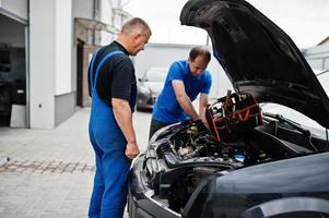 auto reparatie en onderhoud thema. twee monteurs in uniform werken in autoservice, motor controleren. foto