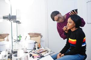 Afro-Amerikaanse vrouw die make-up toepast door visagist bij beauty salon. foto