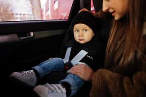 jonge moeder en kind in auto. kinderzitje op stoel. veiligheid rijden concept. foto