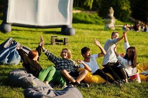 jonge multi-etnische groep mensen kijken naar film op poef in openluchtbioscoop. foto