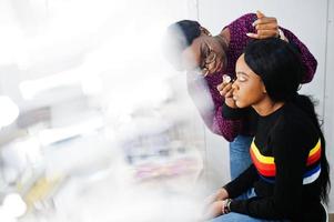 Afro-Amerikaanse vrouw die make-up toepast door visagist bij beauty salon. foto