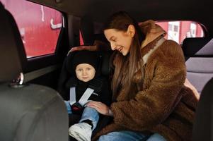 jonge moeder en kind in auto. kinderzitje op stoel. veiligheid rijden concept. foto