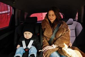 jonge moeder en kind in auto. kinderzitje op stoel. veiligheid rijden concept. foto