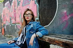 stijlvolle casual hipster meisje in jeans slijtage en bril tegen grote graffiti muur. foto