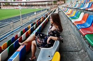 portret van een mooi meisje in jurk en zonnebril zittend op de tribunes in het stadion. foto