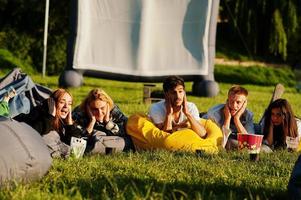 jonge multi-etnische groep mensen kijken naar film op poef in openluchtbioscoop. foto