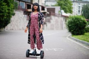 mooie afrikaanse amerikaanse vrouw die segway of hoverboard gebruikt. zwarte meid op zelfbalancerende elektrische scooter met twee wielen. foto