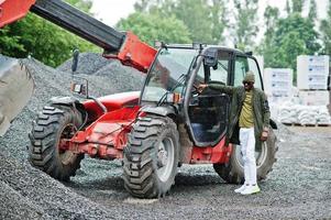 stijlvolle Afro-Amerikaanse man in hoed en zonnebril poseerde buiten in de regen tegen tractor met een emmer. foto