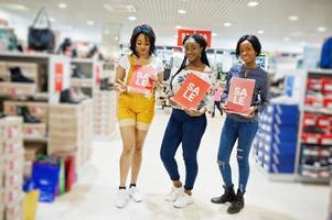 mooie drie goed geklede afro-amerikaanse meisjes bij schoenenwinkel met verkoopborden. foto