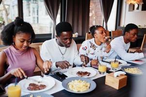 gelukkige afrikaanse vrienden zitten, kletsen in café en eten eten. groep zwarte mensen die in restaurant samenkomen en dineren. foto