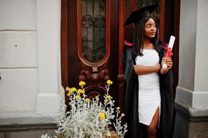 jonge vrouwelijke Afro-Amerikaanse student met diploma poseert buitenshuis.