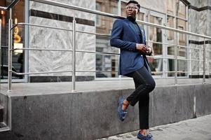 verbazingwekkend uitziende Afro-Amerikaanse man draagt een blauwe blazer met broche, zwarte coltrui en een bril op straat. modieuze zwarte man. foto