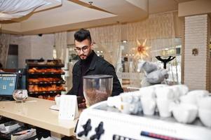 arabische man draagt een zwarte spijkerbroek en een bril in café drinkt koffie aan de bar met boek. stijlvolle en modieuze Arabische modelman. foto