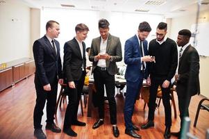 zes multiraciale zakenmannen die op kantoor staan en mobiele telefoons gebruiken. diverse groep mannelijke werknemers in formele kleding met mobiele telefoons. foto