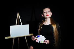 mooie vrouw kunstenaar schilder met borstels en olie canvas poseren in studio geïsoleerd op zwart. foto