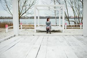 portret van brunette meisje in grijze jurk zit op witte houten constructie. foto