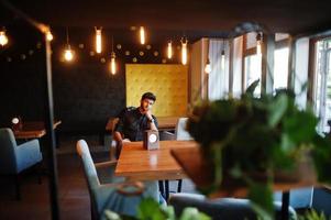 zelfverzekerde jonge Indiase man in zwart shirt zit in café. foto