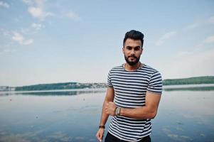 knappe lange arabische baard man model op gestript shirt poseerde buiten tegen het meer en de lucht. modieuze Arabische man. foto