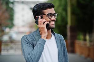 stijlvolle indiase man met een bril draagt casual buiten en spreekt aan de telefoon. foto