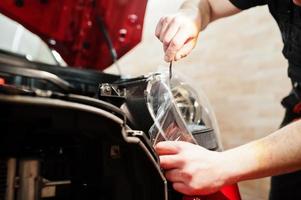 autoservicemedewerker plaatste anti-grindfilm op een rode carrosserie in de detailleringsvoertuigwerkplaats. autobescherming met speciale folies. foto